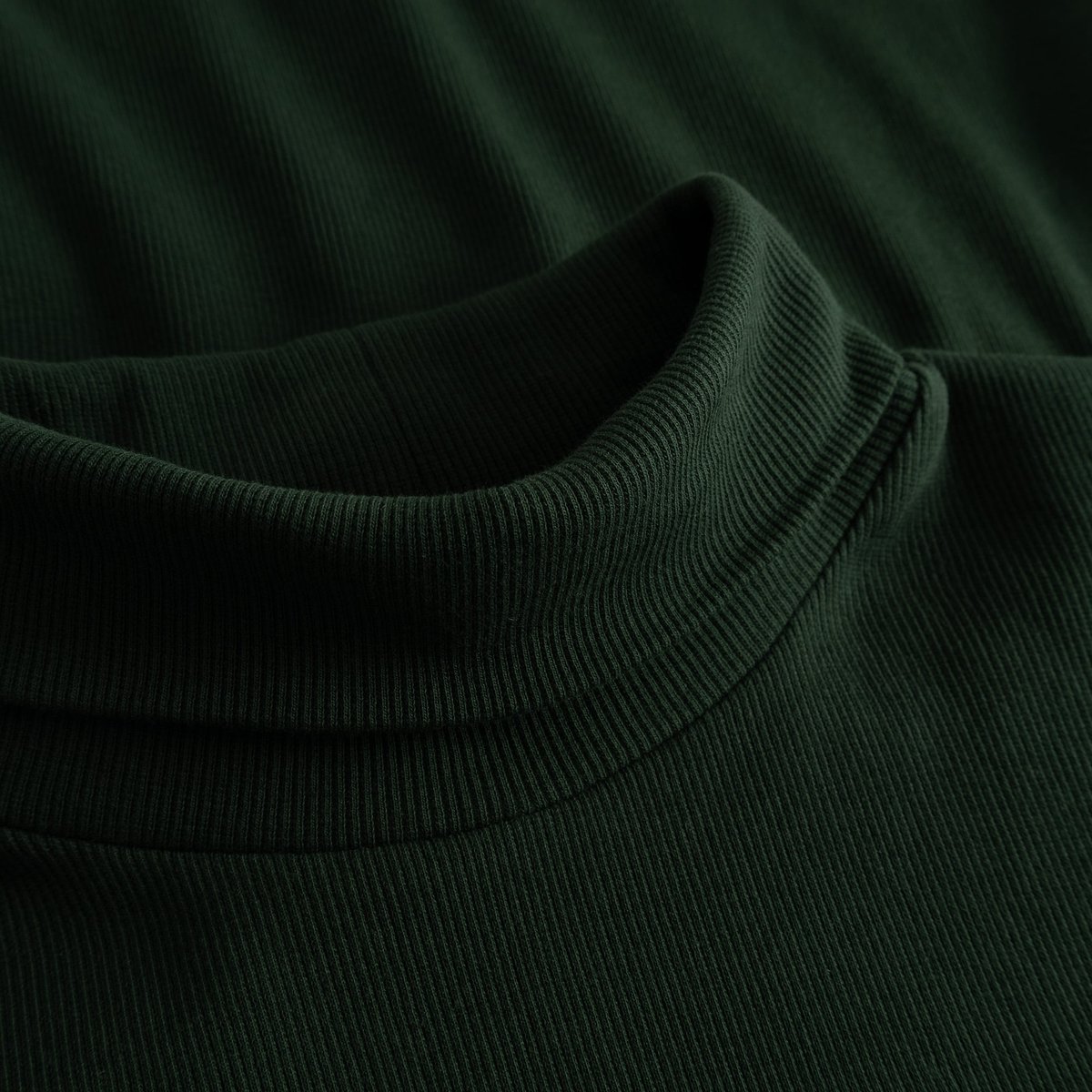 A detailed close-up of the Rib Top Malma in dark green, showing the soft ribbed texture and cozy turtleneck collar.