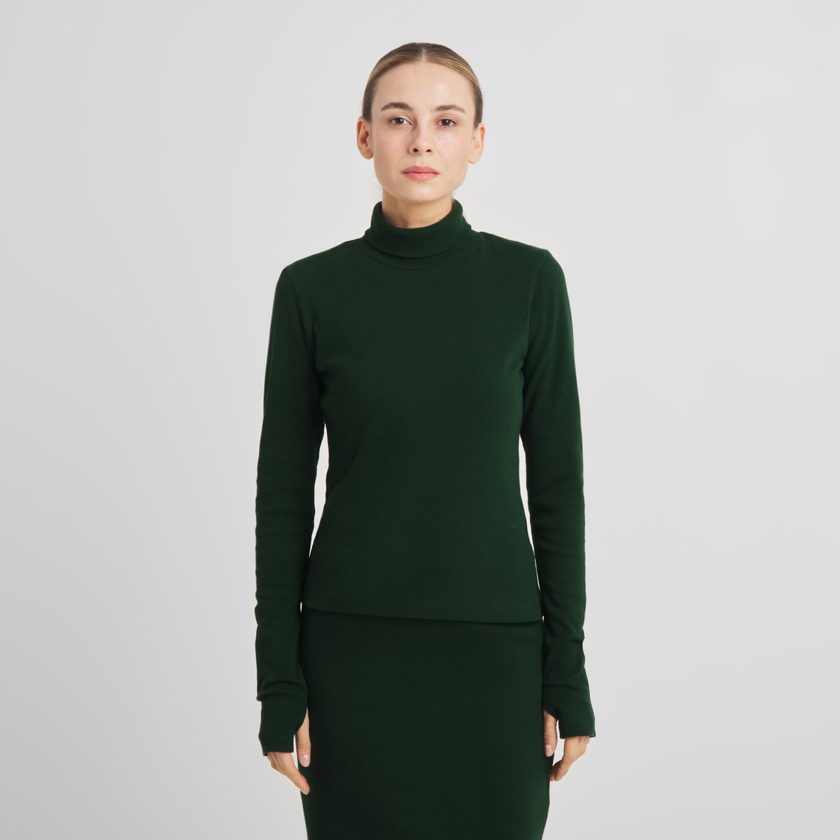 Front view of a model wearing the dark green Rib Top Malma, a slim turtleneck with long sleeves featuring thumbholes.
