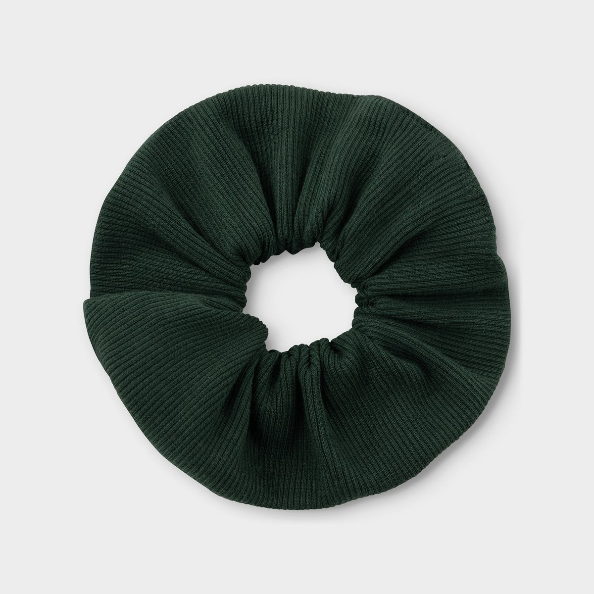 A dark green scrunchie with a ribbed texture, seen from above on a light background.
