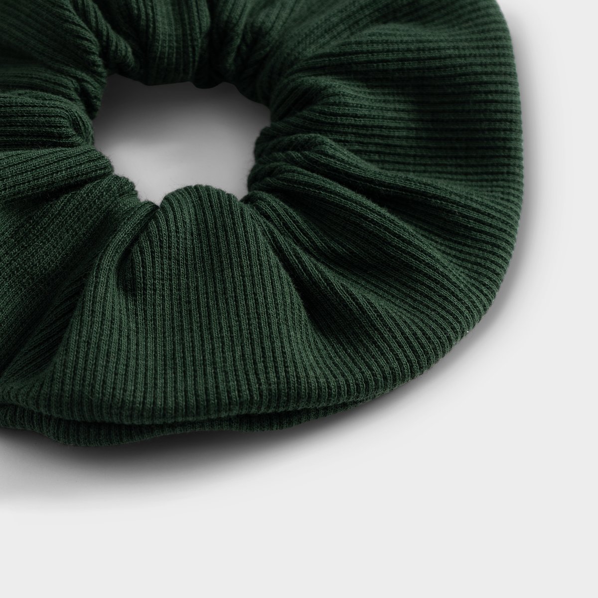 Close-up of the dark green ribbed scrunchie, highlighting the soft texture of the fabric.