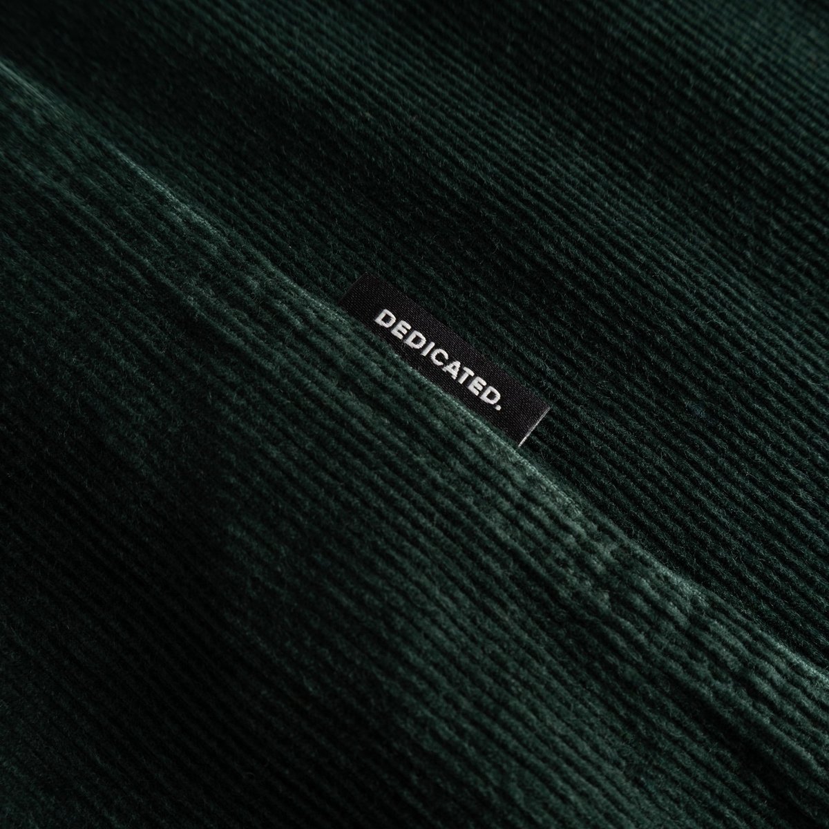 Close-up of the Shirt Varberg Corduroy in dark green, showing the fine texture and the small Dedicated brand label.