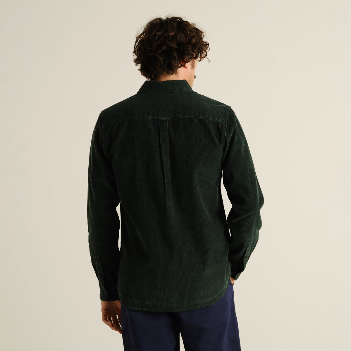 Model with curly hair seen from behind, wearing the Varberg Corduroy Shirt in a deep dark green.