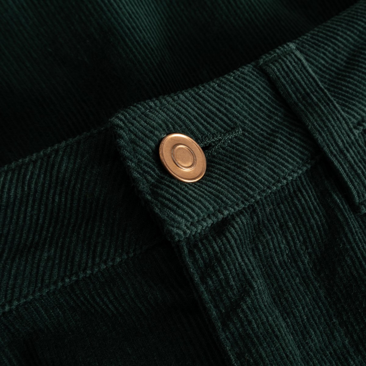 Detailed shot of the Pants Ryda Corduroy in dark green, highlighting the fine cord fabric and classic bronze-colored button.