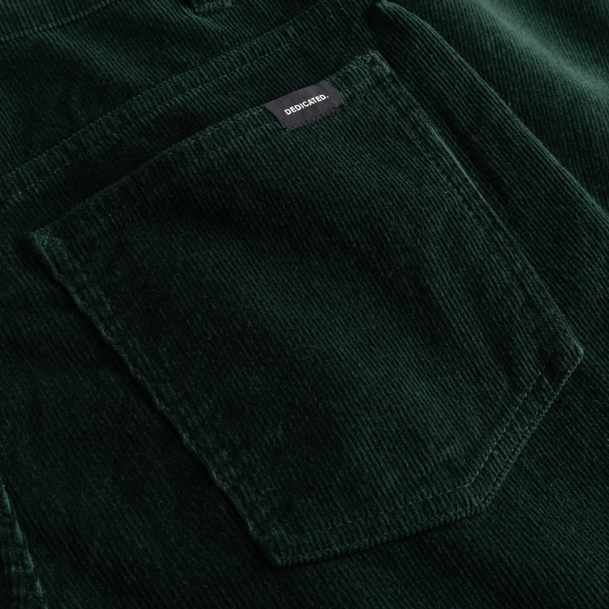 A close-up of the back pocket on the Pants Ryda in Dark Green, showcasing the rich corduroy texture and the Dedicated label.
