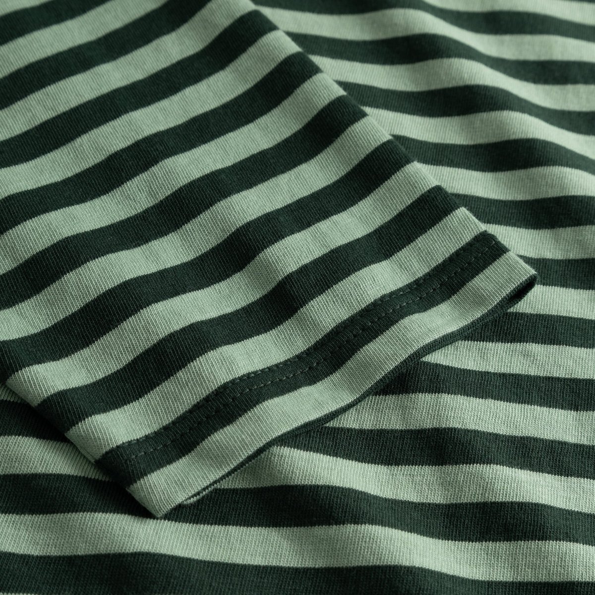 A detailed close-up of the sleeve on the Top Humledal, showing the dark green and granite green striped organic cotton.