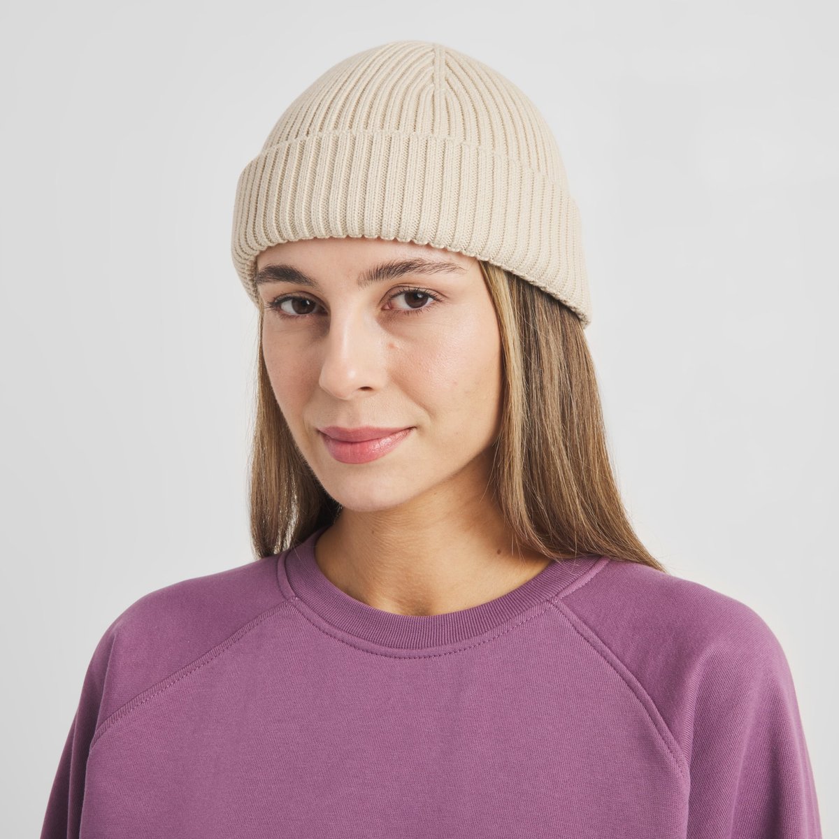 A close-up of a woman wearing the short, ribbed-knit Beanie Rutvik in Oat White against a light studio background.