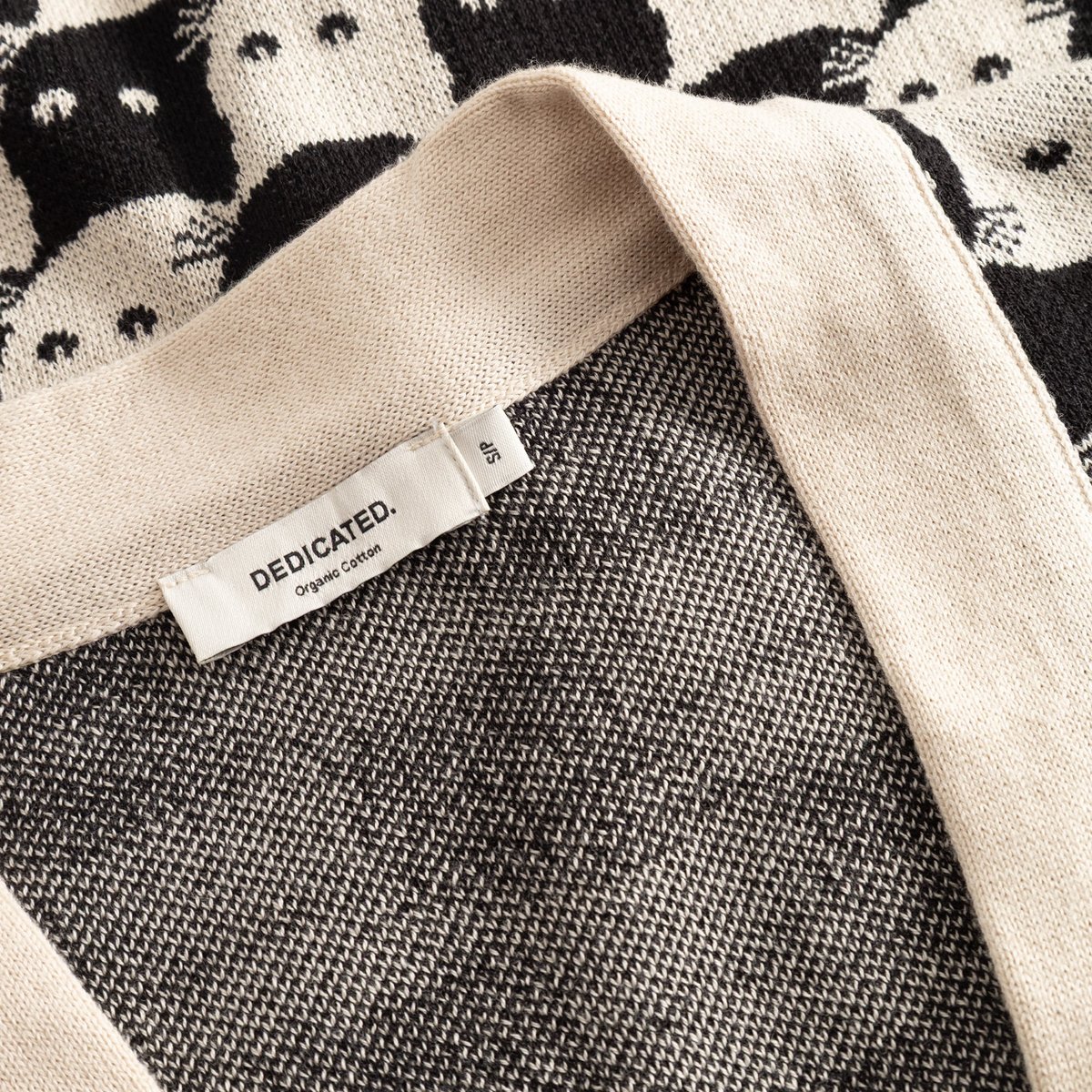Detailed close-up of the oat white Kanan Cardigan, showing the Dedicated brand label and the cute Pepita Cats jacquard knit.