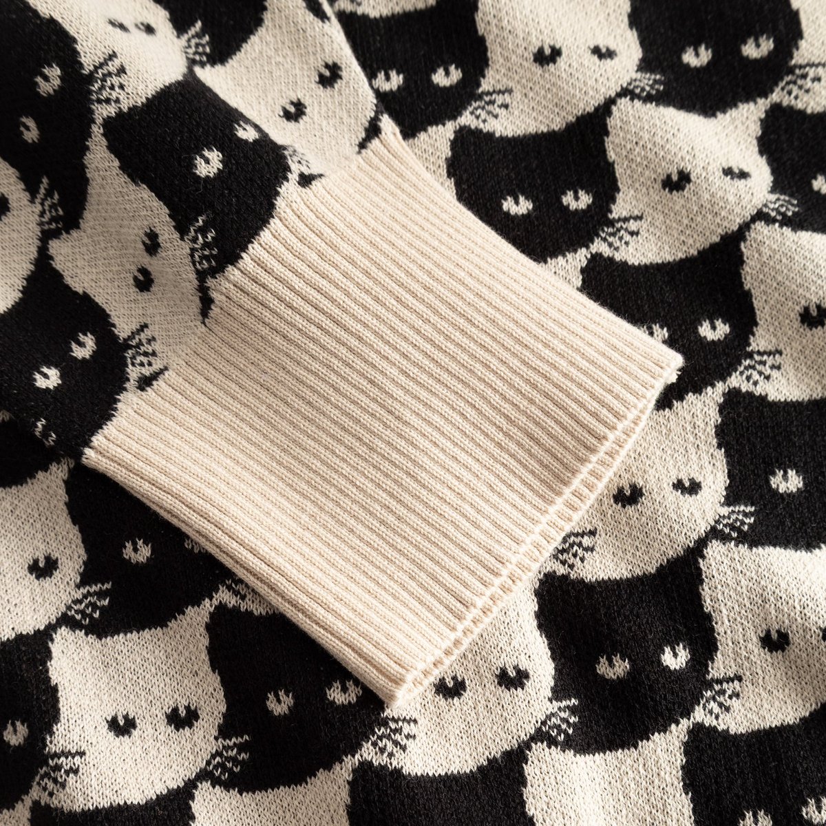 Close-up of the oat white ribbed cuff on the Cardigan Kanan, set against the playful black and white jacquard cat pattern.