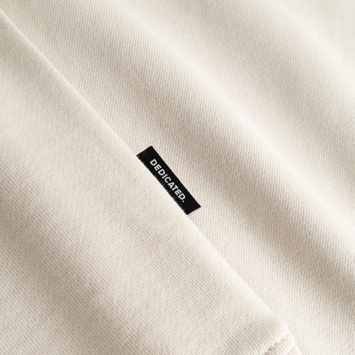Close-up shot of the oat white Sweatshirt Malmoe, highlighting the soft fabric and the black Dedicated brand tag on the seam.