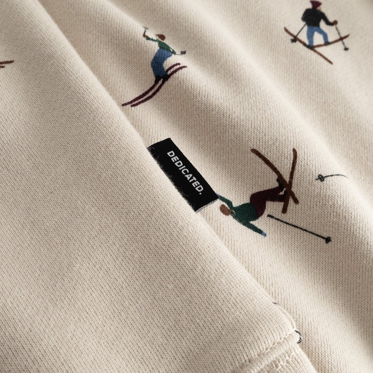Close-up of the oat white Hoodie Falun Ski Team, featuring the all-over skier print and the black Dedicated brand tag.