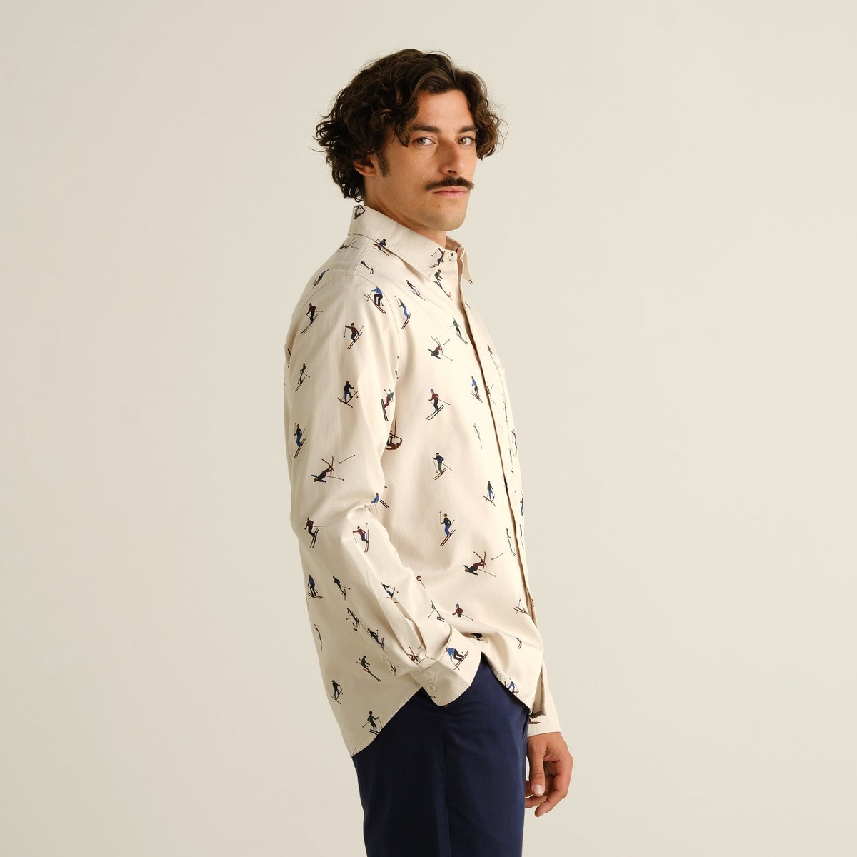 Side view of a man wearing the fun Shirt Lunnevik Ski Team in Oat White with navy trousers.