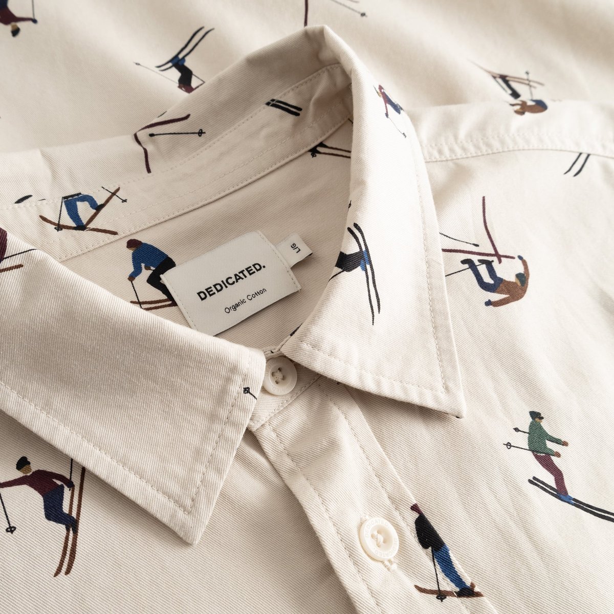 A close-up of the collar on the Shirt Lunnevik Ski Team in Oat White, showing the fun skier print and the Dedicated label.