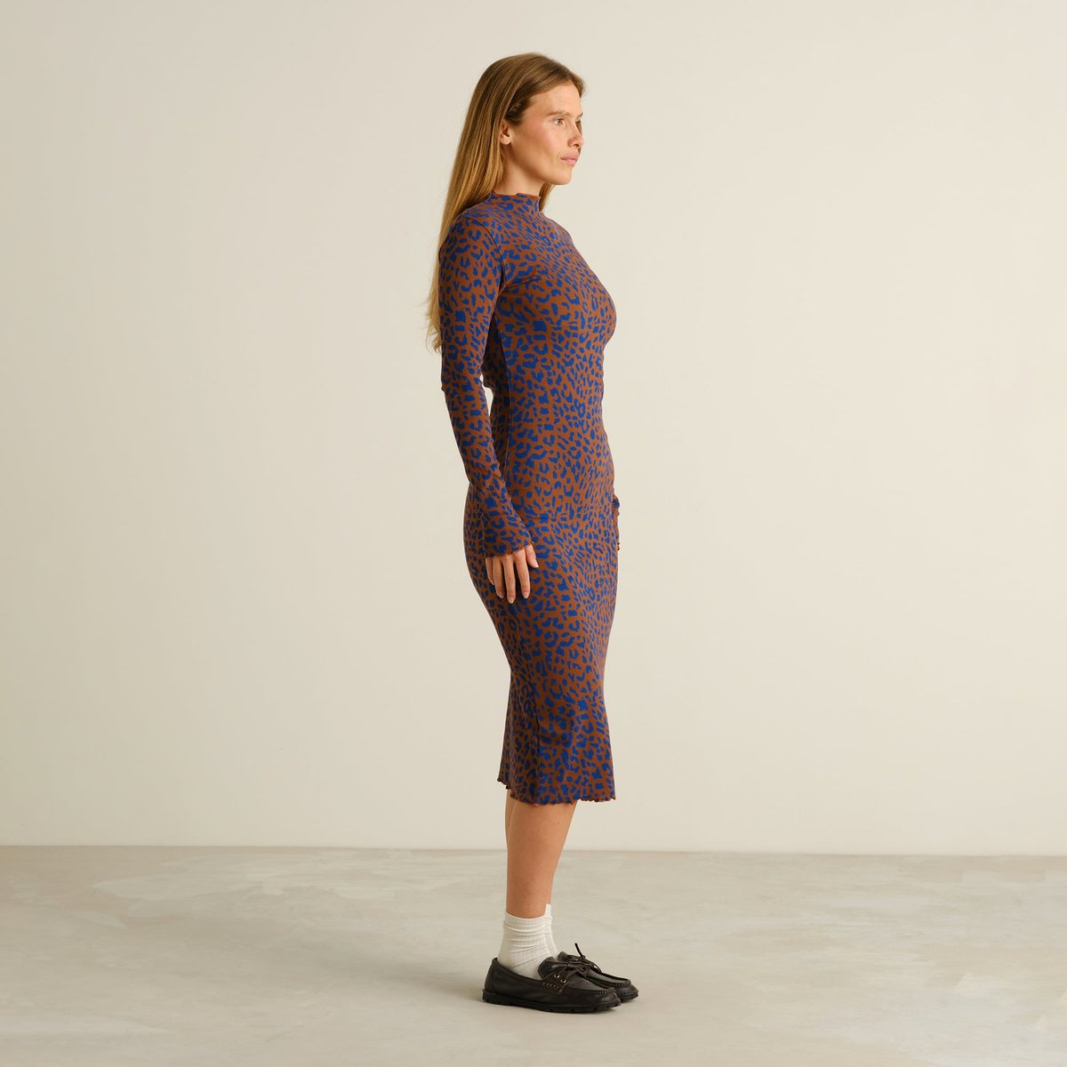 Full side profile of a woman wearing the long-sleeved Rib Dress Lofta in a bold brown and blue leopard print.