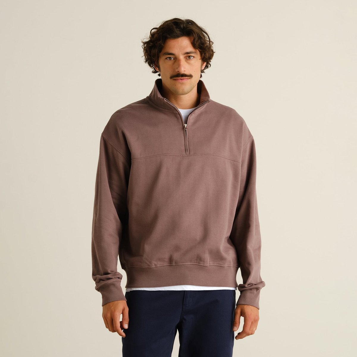 A man looks at the camera while wearing the relaxed-fit Half Zip Sweatshirt Sandvalla in Sparrow Brown.