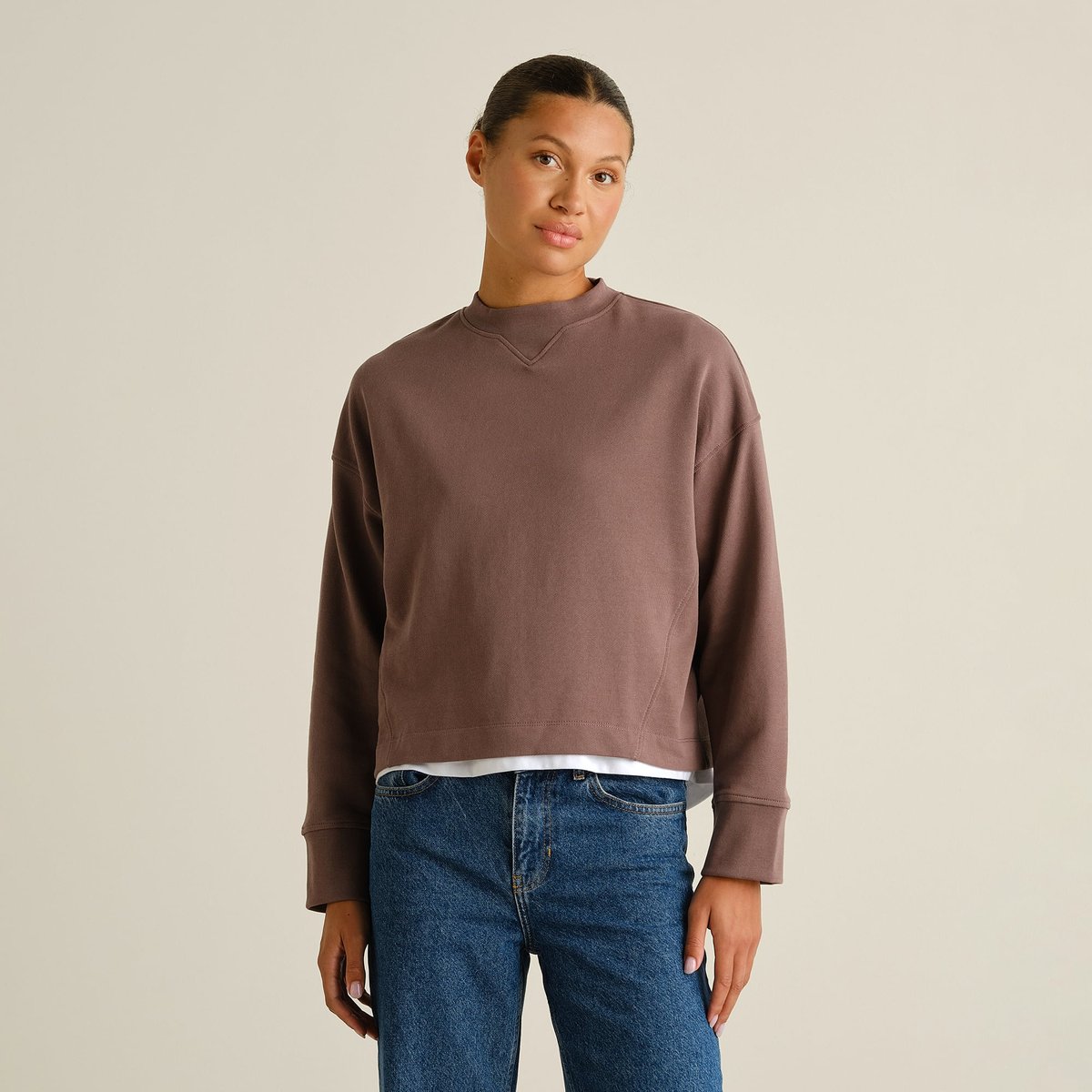 A model wears the Sweatshirt Gia in Sparrow Brown, styled simply with a white t-shirt and classic blue jeans.