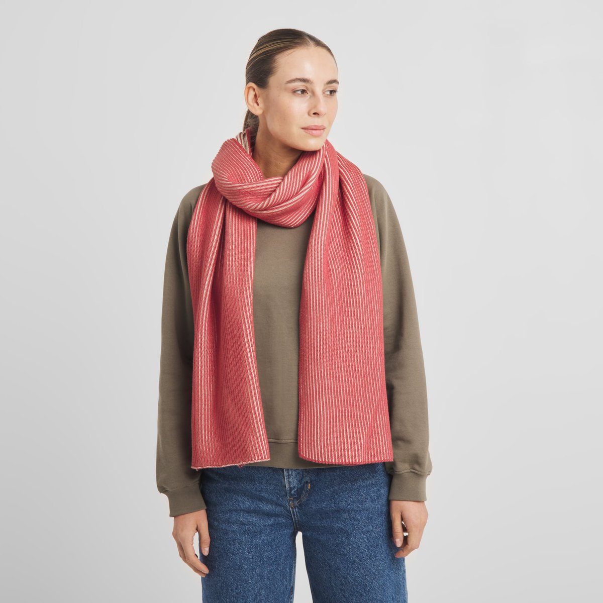 En modell bär den tvåfärgade halsduken Norrfors Brioche i Vanilla White och Holly Red, stylad med en ledig sweatshirt.
