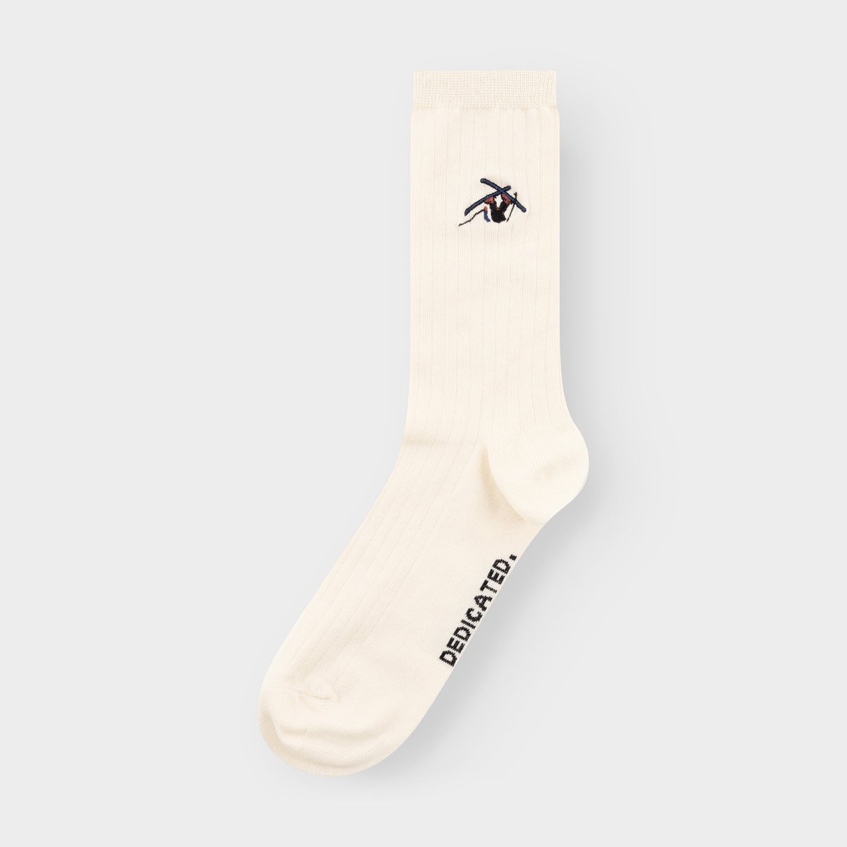 En off-white ribbad strumpa med en broderad skidåkare som vurpar, fotad mot en ljusgrå bakgrund.