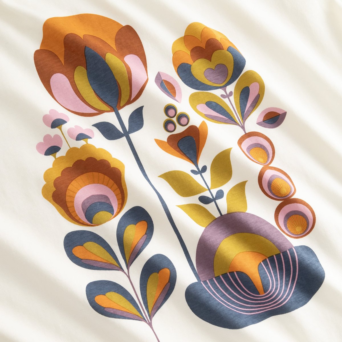 Close-up of the T-shirt Vadstena 'Autumn Harvest' print, a retro floral design in warm autumnal colors on an off-white base.