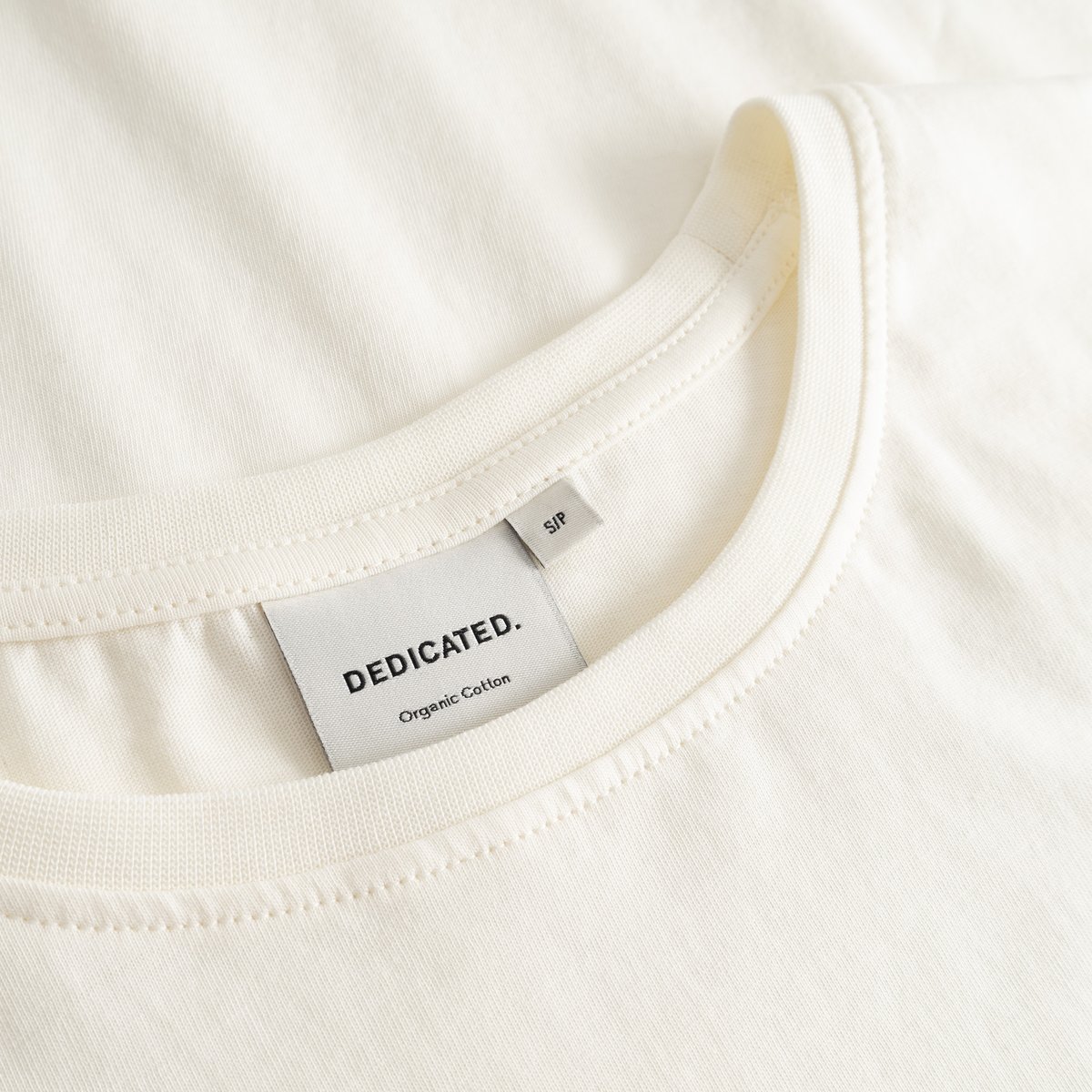 Close-up of the neckline and brand label on the T-shirt Visby Watercolor Cat in off-white organic cotton.