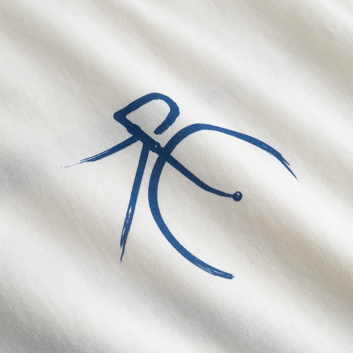 Close-up of the T-shirt Stockholm in Off-White, showing the artistic brush-stroke detail of the blue bicycle graphic.