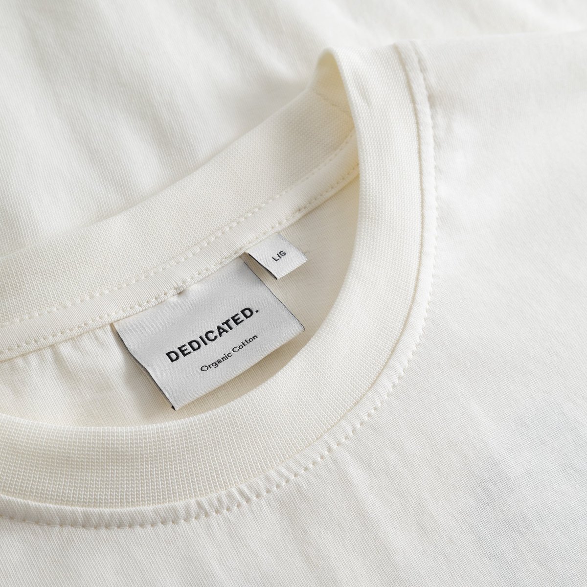A detailed close-up of the ribbed crew neck and brand label on the off-white T-shirt Stockholm Camp Crew.