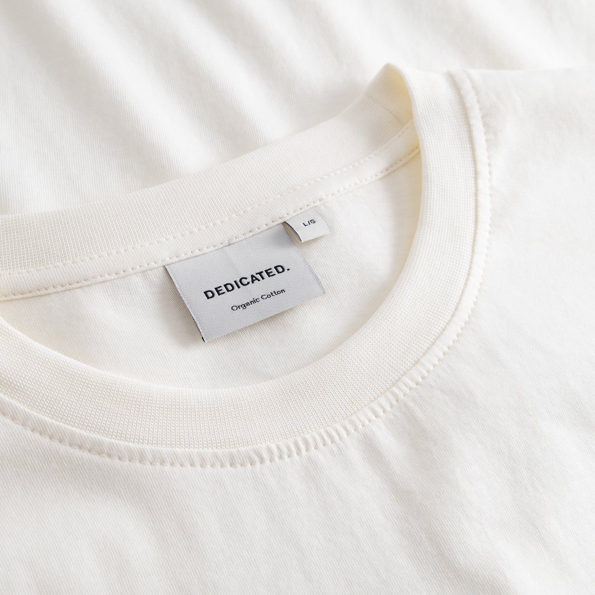 Close-up detail shot of the brand label and soft ribbed collar on the T-shirt Stockholm Karaoke Killer in off-white.