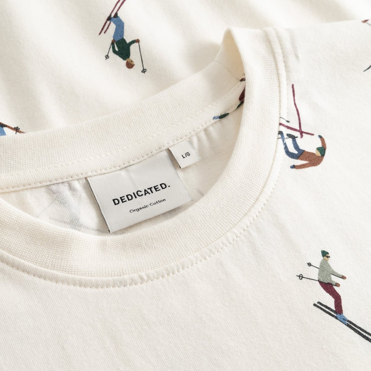 Close-up of the Dedicated Ski Team t-shirt in off-white, showing the ribbed collar and fun all-over skier print.