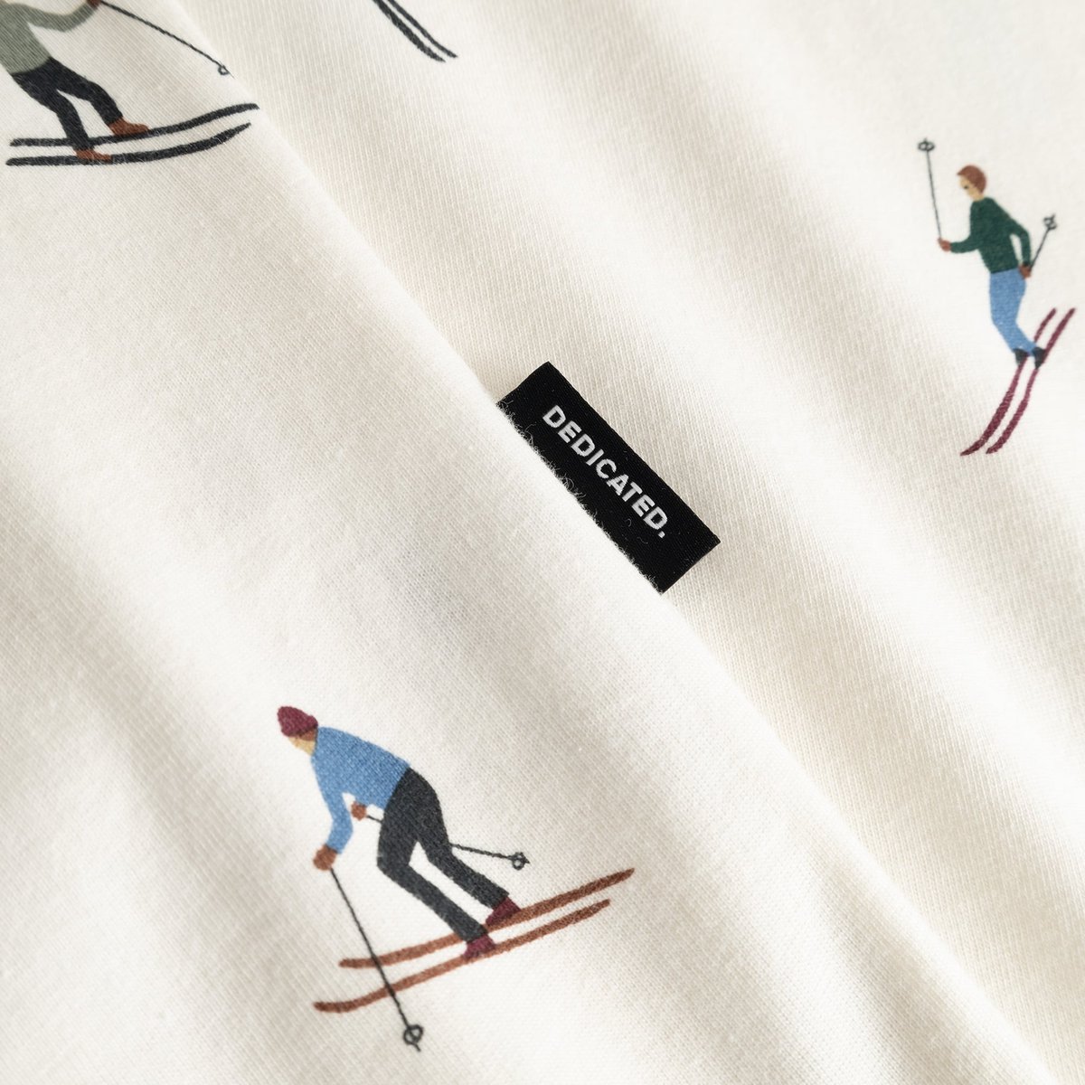 A close-up of the off-white Stockholm Ski Team t-shirt's fabric, showing the skier print and Dedicated brand tag.