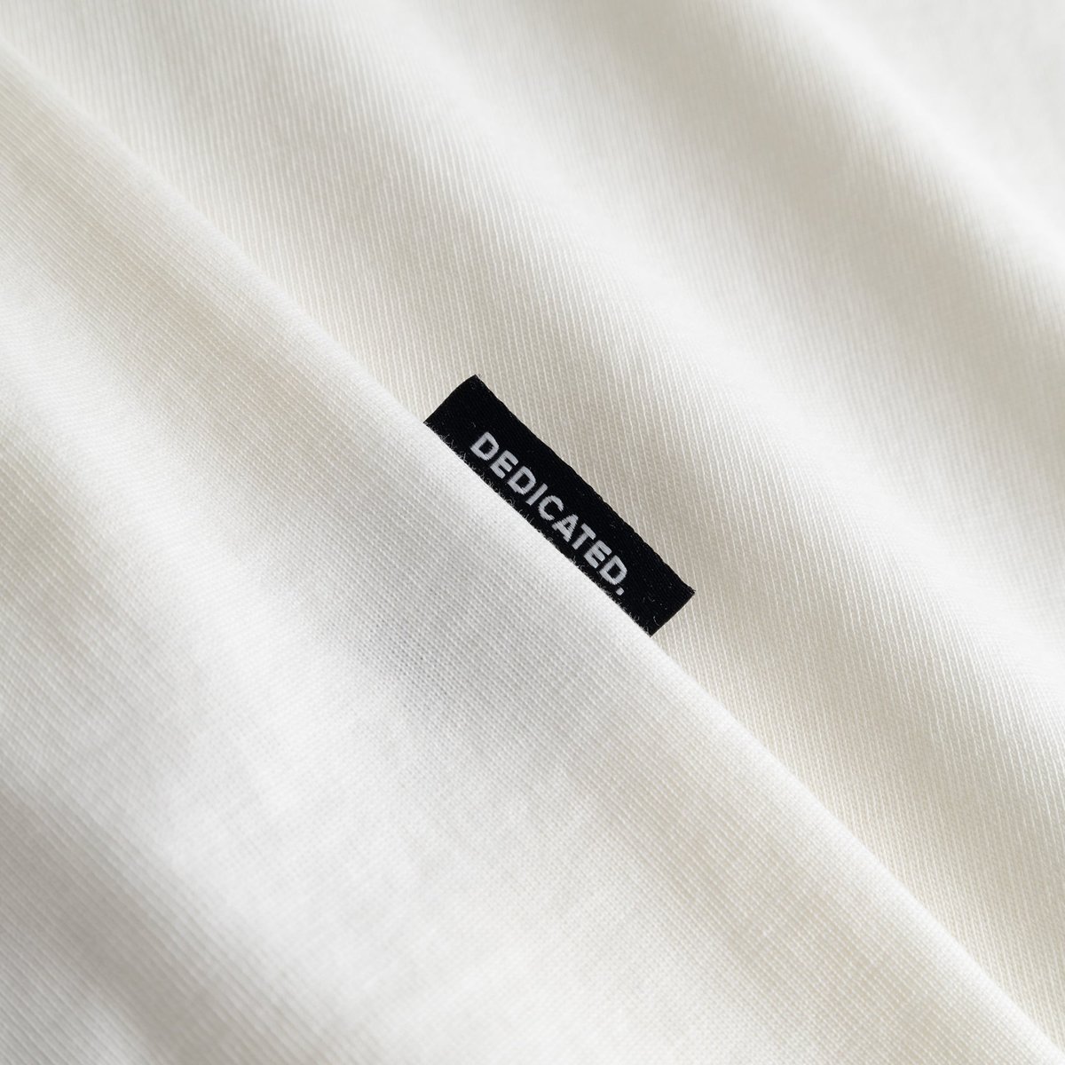 Close-up of the soft off-white fabric on the T-shirt Stockholm, featuring the signature black Dedicated brand tab.