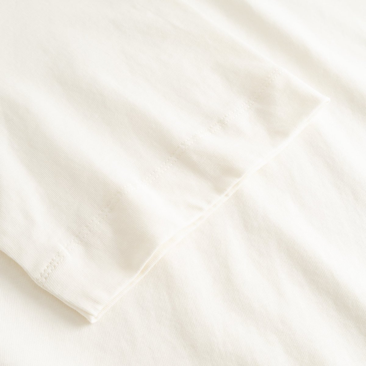 Close-up of the finely stitched sleeve on the T-shirt Vadstena in soft, off-white organic cotton.