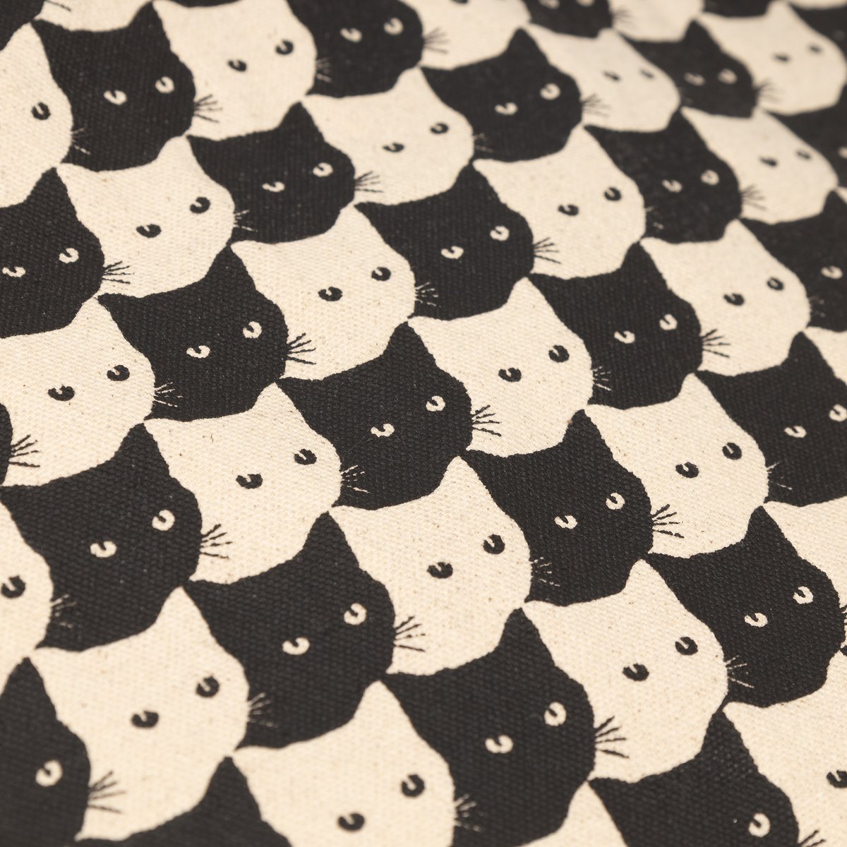 Close-up of the Tote Bag Torekov's sturdy canvas, featuring a playful, interlocking pattern of black and off-white cat faces.