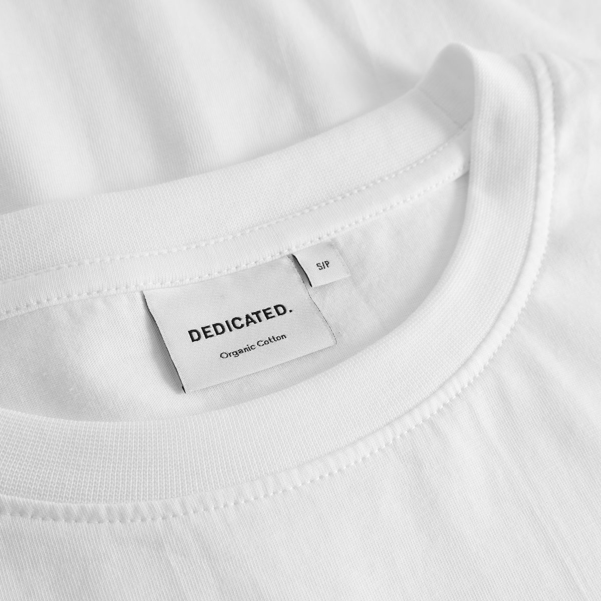 Close-up of the brand label and ribbed collar of the T-shirt Vadstena Lamb in white.