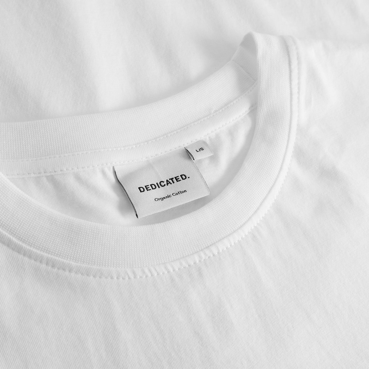 Close-up of the Dedicated label and ribbed collar on the white T-shirt Stockholm Apres Ski Instructor.