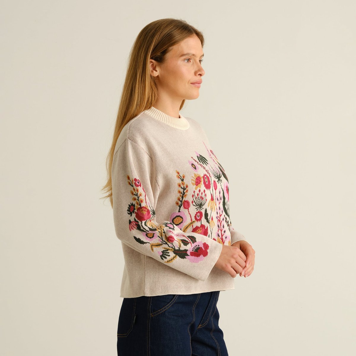 Side profile of a woman wearing the vanilla Sweater Limhamn, featuring a vibrant folk flower design on the body and sleeve.
