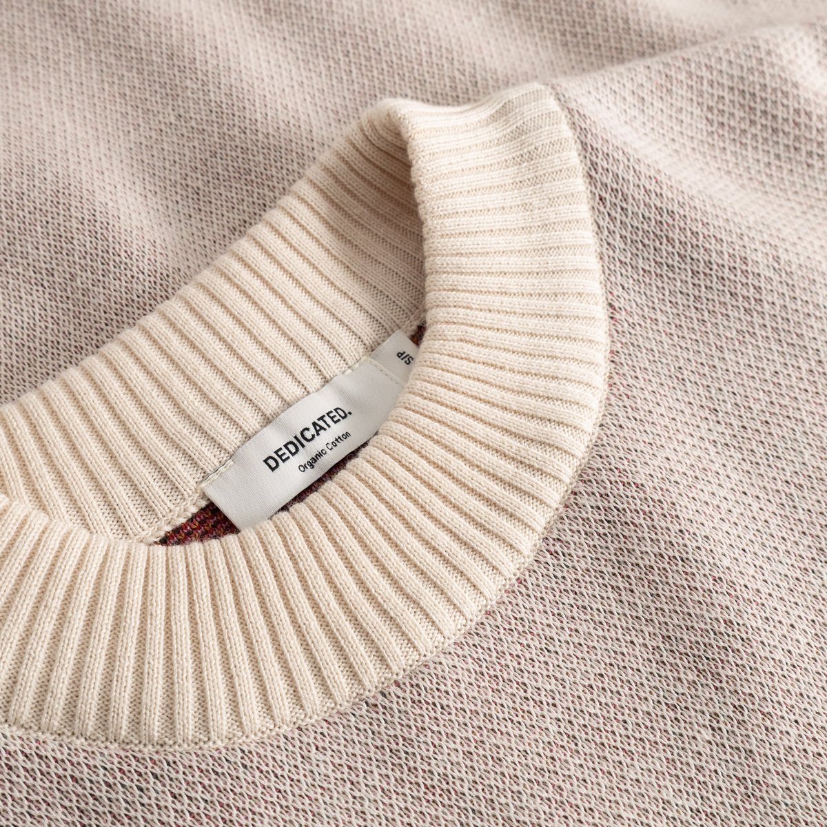 Close-up on the soft ribbed collar and jacquard knit of the vanilla white Limhamn sweater, featuring the Dedicated label.