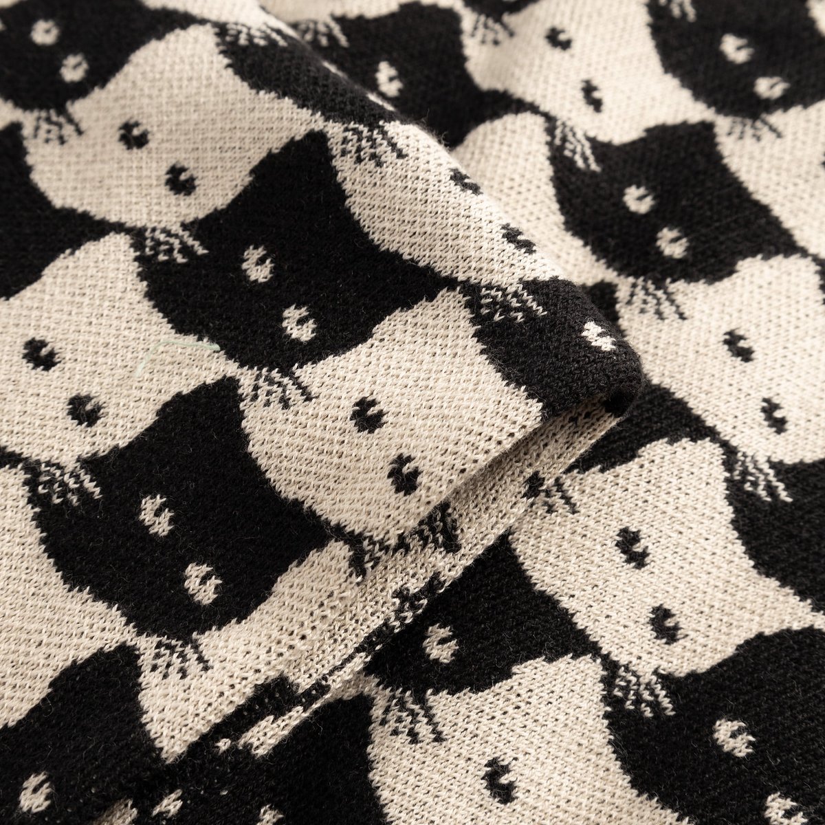 A close-up view of the Scarf Rossberga, showcasing the fine jacquard knit and the playful Pepita Cats pattern in oat white.