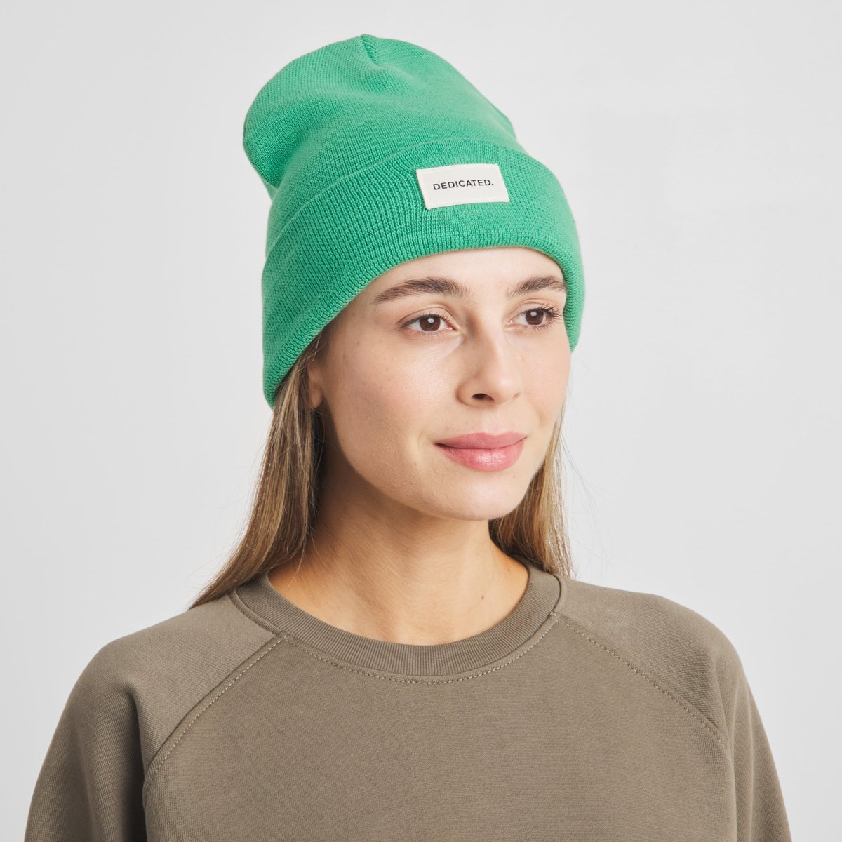 En kvinna ler mjukt i den klargröna mössan Beanie Kiruna Winter Green.