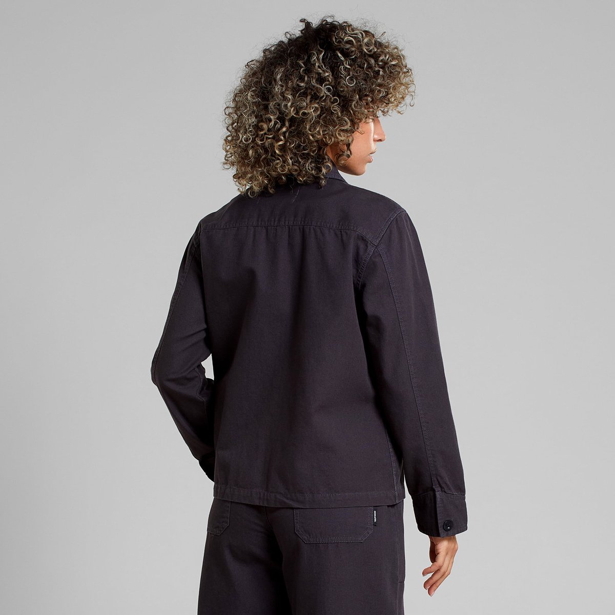 Model with curly hair seen from behind wearing the Jacket Stiby Canvas in Phantom Black, showing off its relaxed fit.
