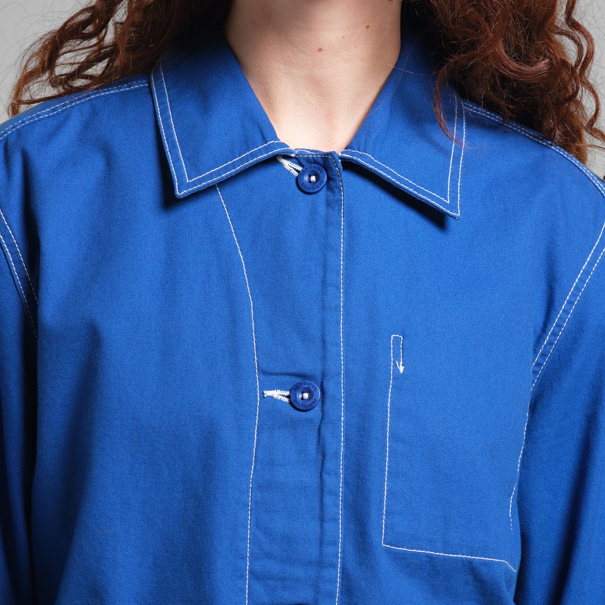 Close-up of a model wearing the blue Stiby Canvas Jacket, showing the collar, buttons, and white contrast stitching detail.