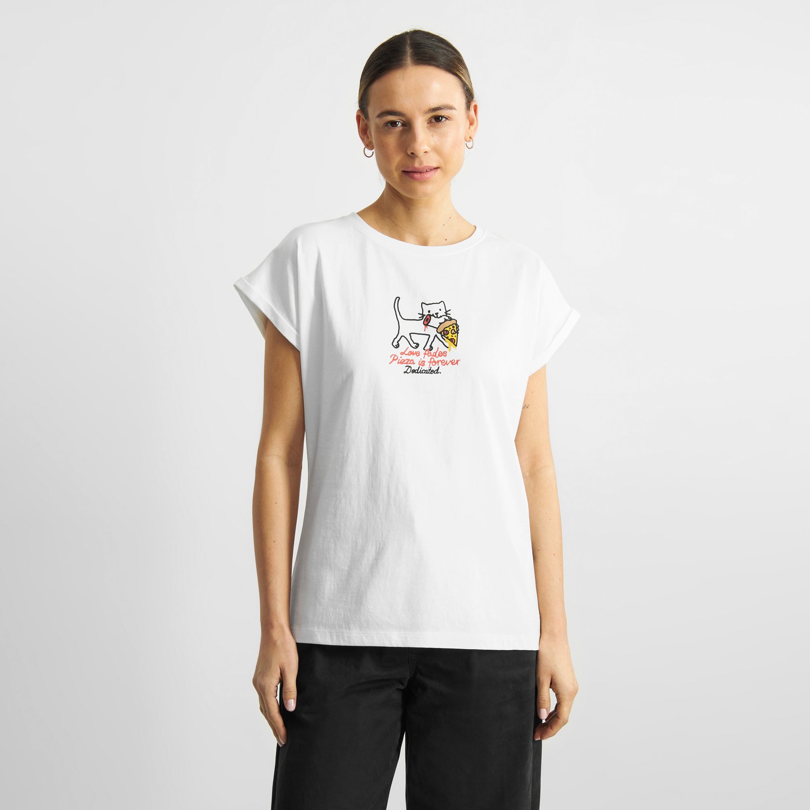 A woman shows off the white T-shirt Visby Pizza Love, featuring a cat and pizza print, worn with black trousers.