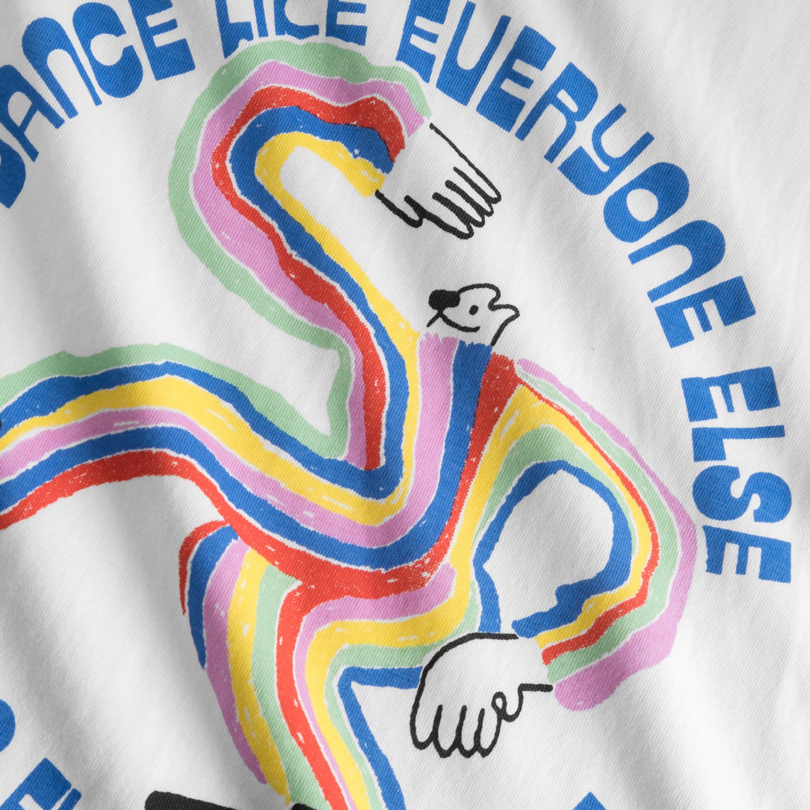 Close-up of the 'Dancing Man' print with a rainbow figure and the blue text 'Dance Like Everyone Else' on a white t-shirt.
