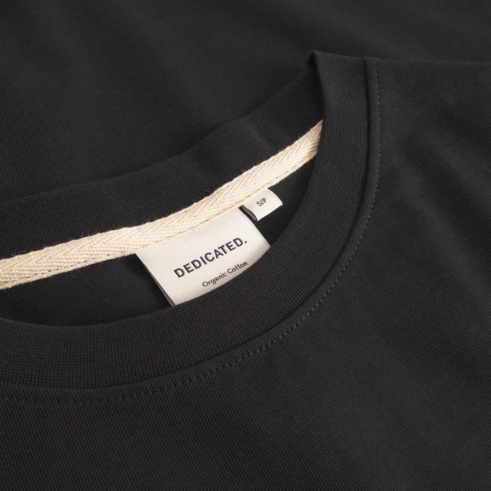 A close-up of the ribbed neckline and Dedicated brand label on the T-shirt Ljusdal in black.