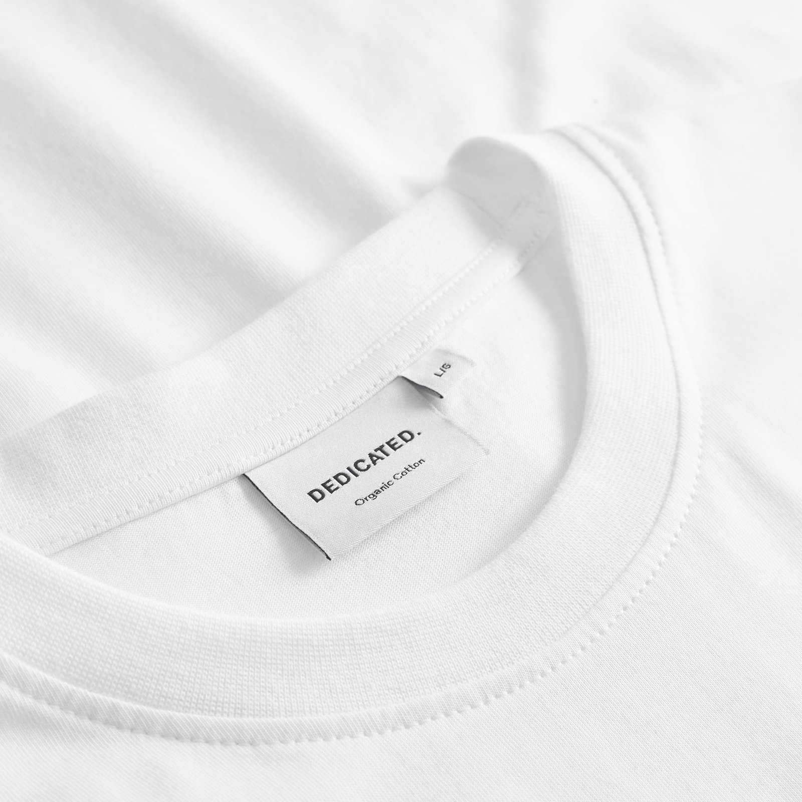 Close-up of the off-white T-shirt Stockholm Beach Habitat's collar, showing the Dedicated brand label.