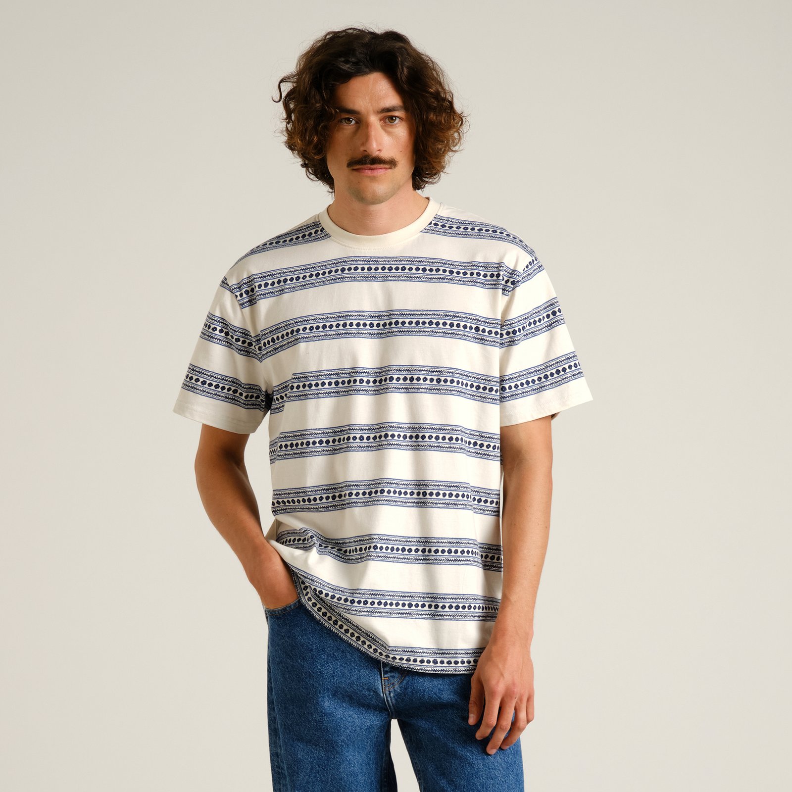 A model with a mustache poses in the off-white and blue Stockholm Floral Stripe T-shirt, casually styled with blue jeans.