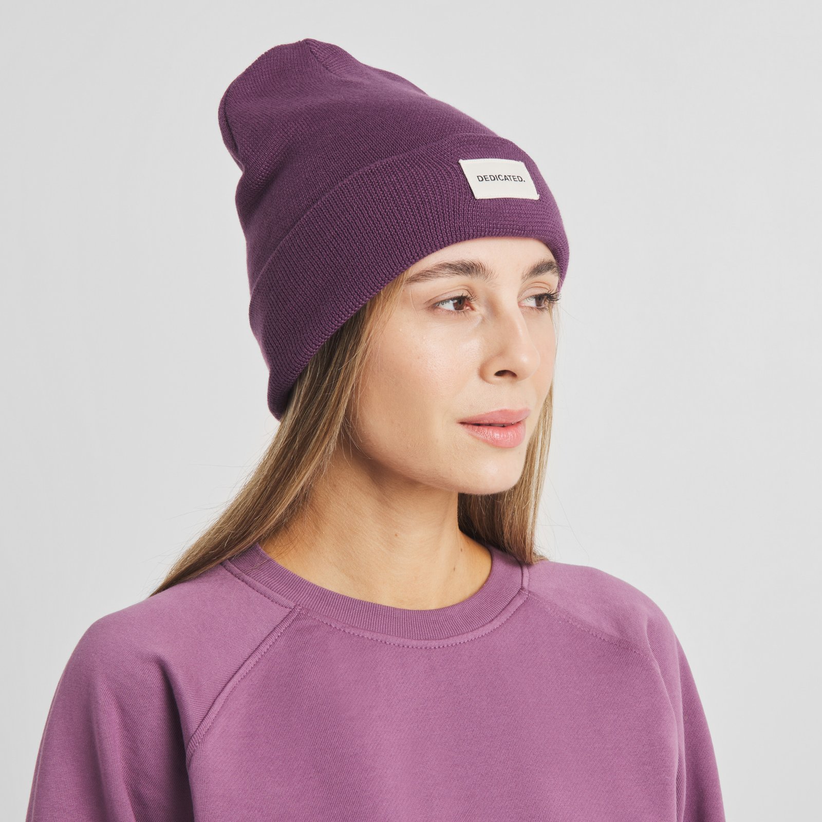 Kvinna som bär den bärlila mössan Beanie Kiruna från Dedicated och tittar åt sidan.