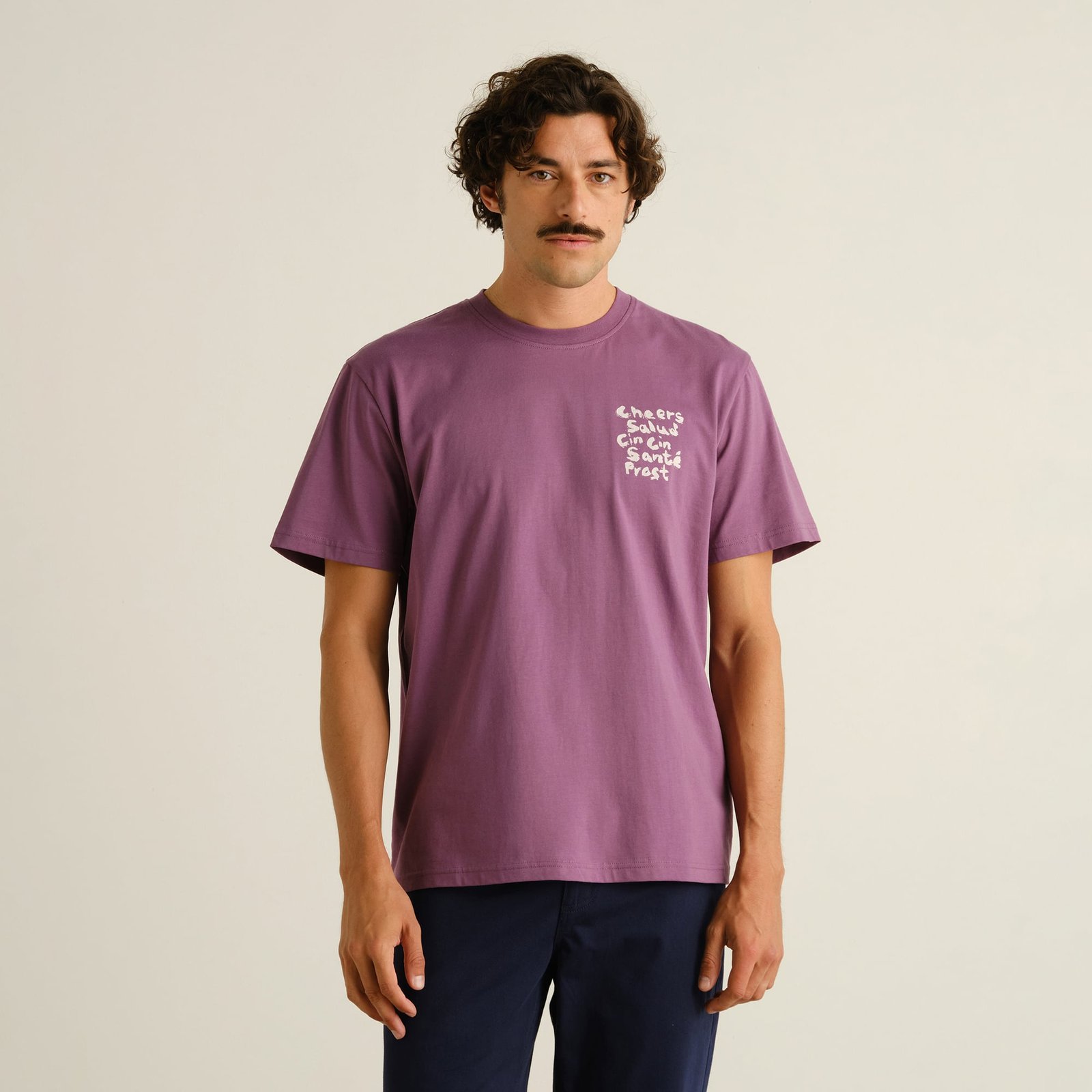 Vorderansicht eines Models, das das beerenlilane T-Shirt Stockholm Cheers Salud zu einer dunklen Hose trägt.