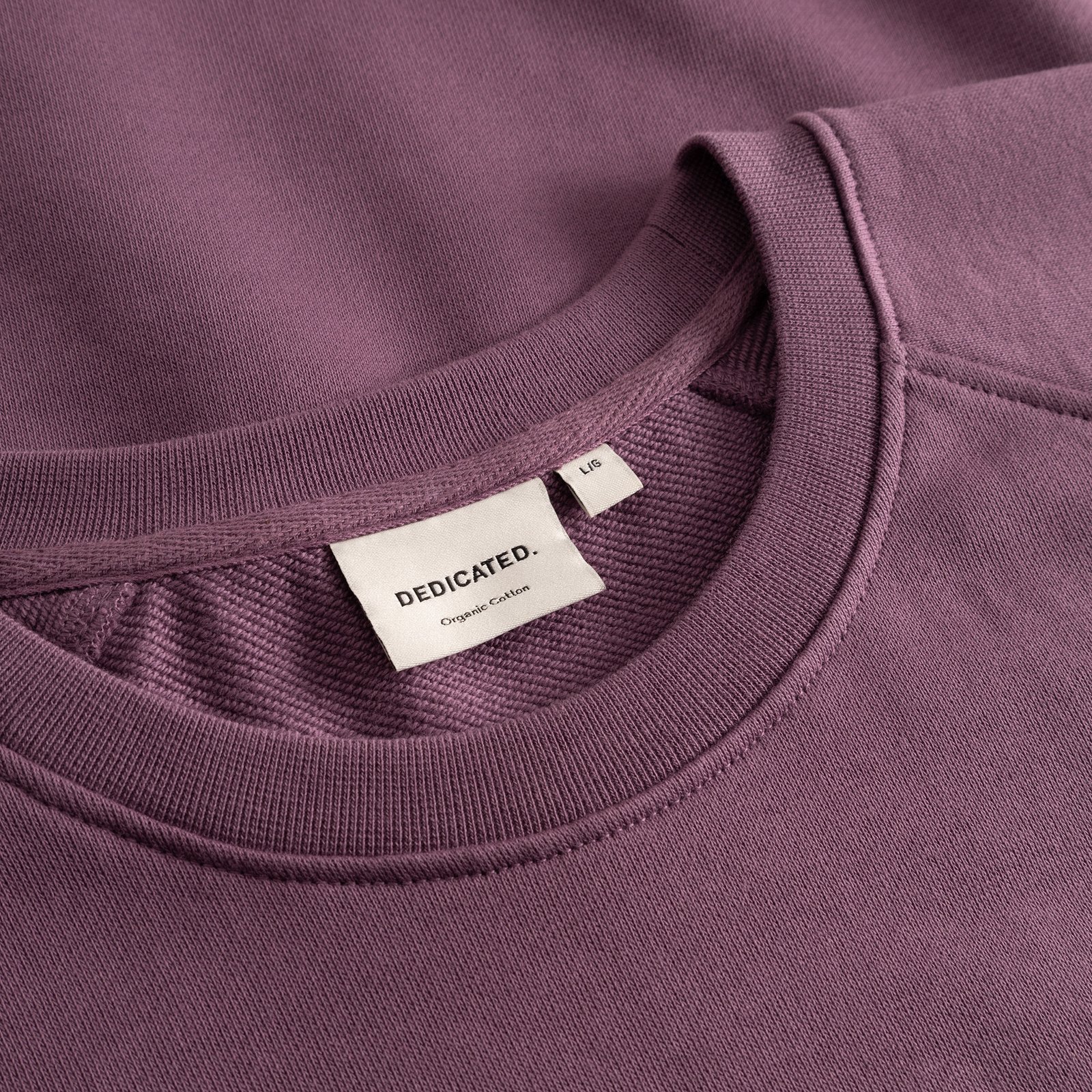 Close-up shot of the Sweatshirt Malmoe Base in Berry Purple, focusing on the ribbed crew neck and the Dedicated brand label.
