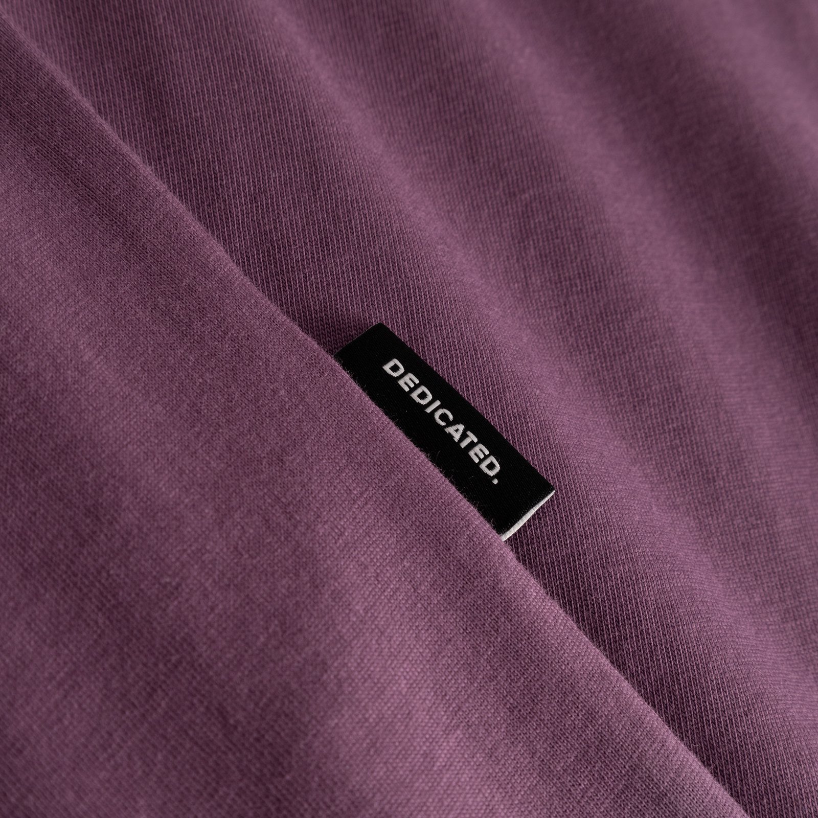 Närbild på T-shirt Stockholm Base i Berry Purple, som visar tygstrukturen och den lilla Dedicated-etiketten.