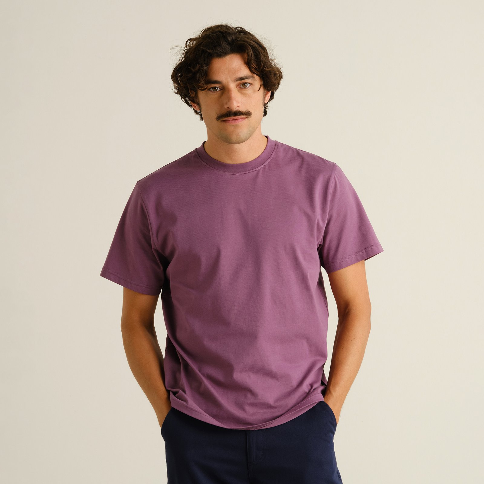 En man poserar avslappnat i den klassiska t-shirten Stockholm Base i en klar, bärlila färg.