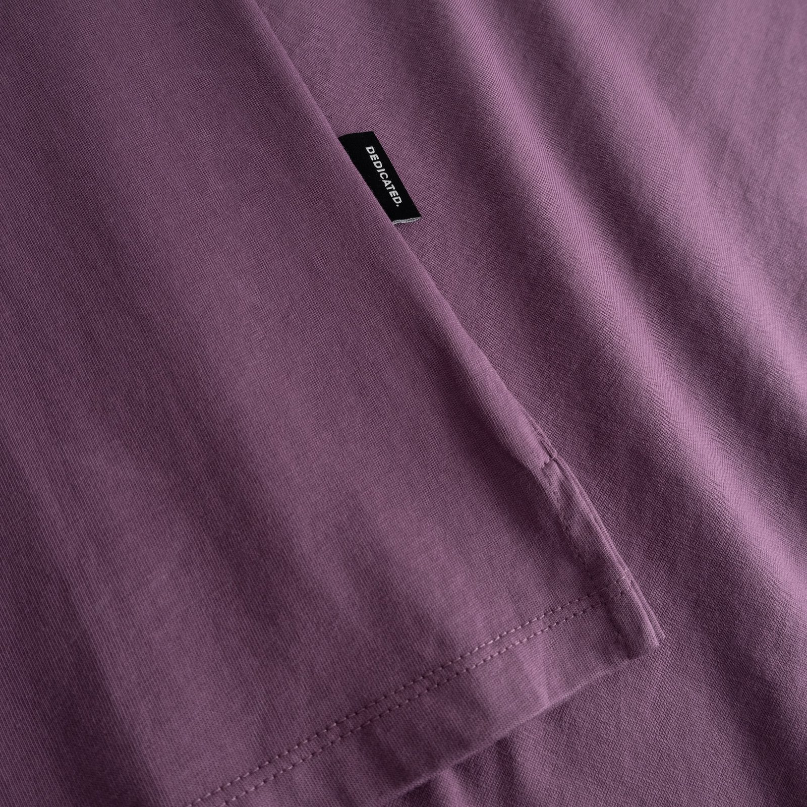 Close-up of the folded sleeve, side slit, and brand tag on the T-shirt Visby Base in a rich Berry Purple hue.